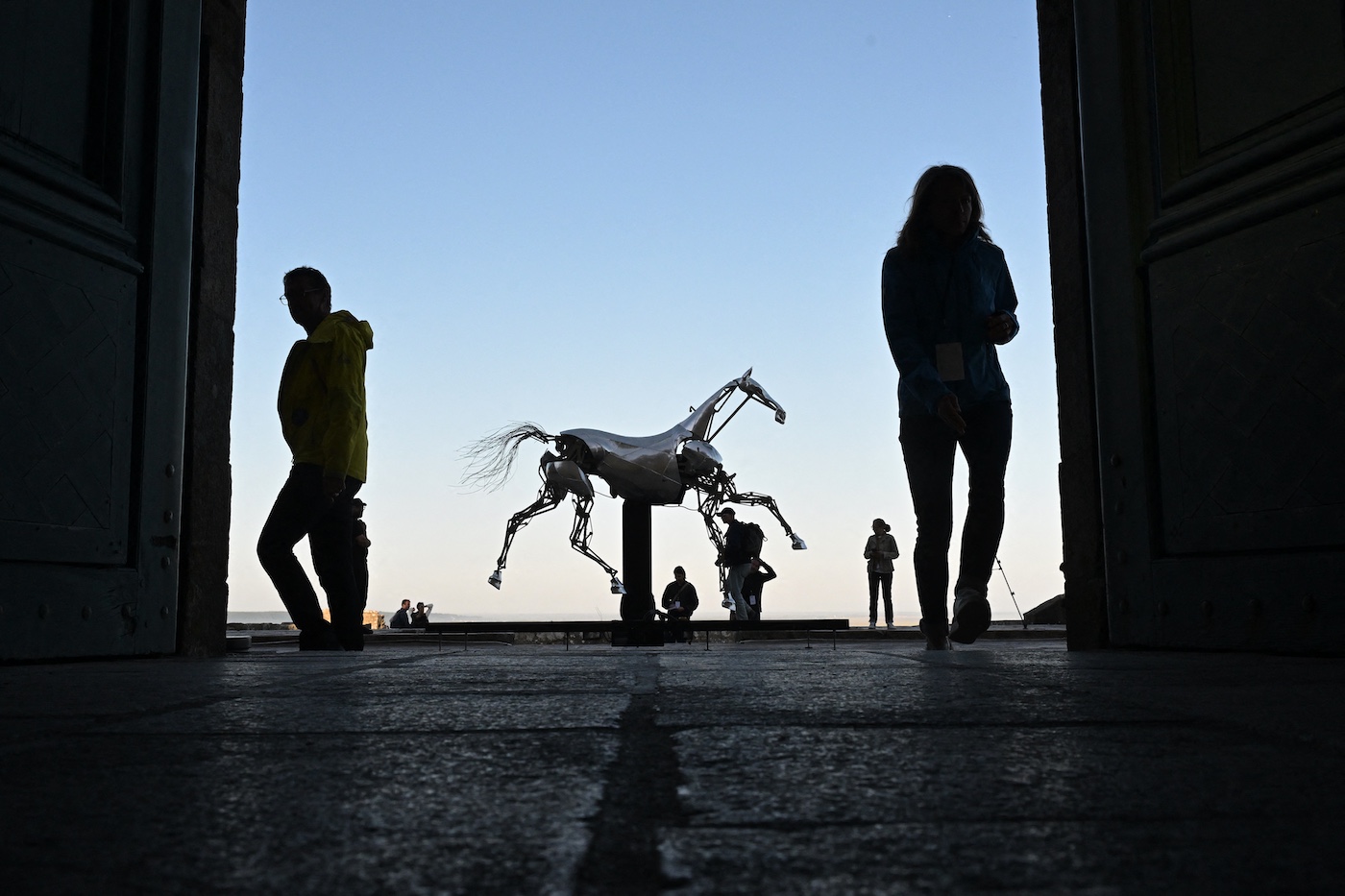 Les invités et les journalistes se tiennent à côté de Zeus, le cheval mécanique utilisé lors de la cérémonie d'ouverture des Jeux olympiques de Paris 2024, après avoir été installé sur la terrasse de l'abbaye du Mont Saint-Michel le 9 juillet 2025. Le cheval emblématique sera exposé jusqu'au 7 septembre 2025. (Photo de Damien Meyer / AFP)